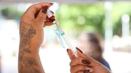 Imagem de arquivo das mãos de uma profissional de saúde aspirando uma dose de vacina de um frasco-ampola para dentro de uma seringa
