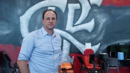 Homem de camisa azul-clara em frente a mural com o escudo do São Paulo Futebol Clube