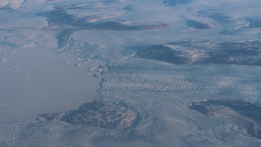 Vista aérea de gelo derretendo na costa da Groenlândia, com água visível sob a camada de gelo