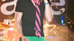 Fiuk cantando em show, com chapéu e calça verde