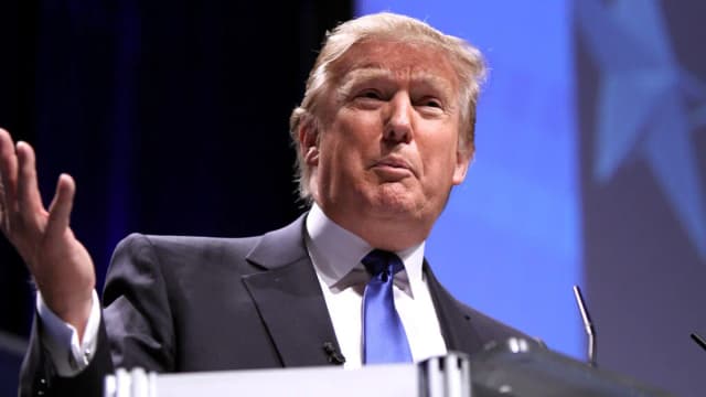 Donald Trump discursa em evento, vestindo terno escuro e gravata azul