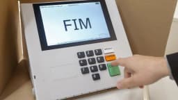 Mão de eleitor digita na urna eletrônica, com tela mostrando a palavra FIM após o voto
