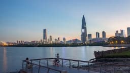 Vista do horizonte de arranha-céus de Shenzhen, na China, ao entardecer, com pessoas em um calçadão à beira do rio