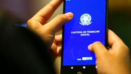 Mãos de uma pessoa segurando um celular com o aplicativo da Carteira de Trabalho Digital aberto na tela