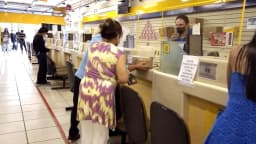 Cliente é atendida no balcão de uma agência dos Correios, com funcionário ao fundo