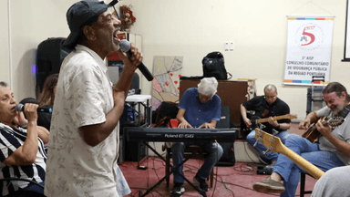 Hamilton Assunção canta ao microfone durante ensaio da banda Harmonia Enlouquece no Centro Psiquiátrico do Rio de Janeiro, cercado por outros integrantes tocando teclado e violão