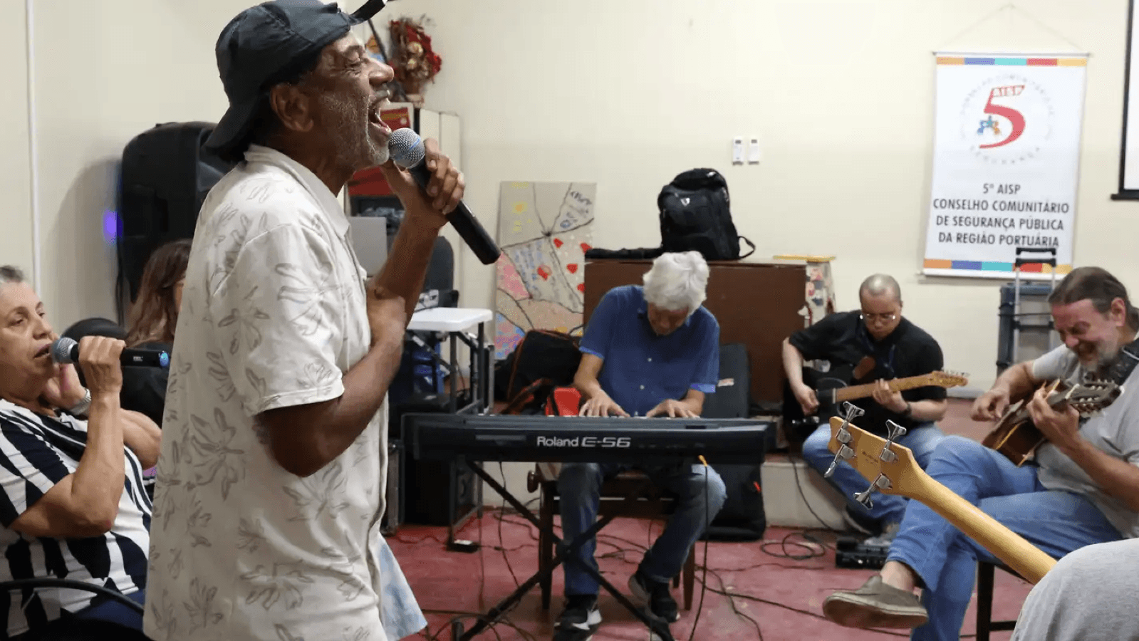 Hamilton Assunção canta ao microfone durante ensaio da banda Harmonia Enlouquece no Centro Psiquiátrico do Rio de Janeiro, cercado por outros integrantes tocando teclado e violão