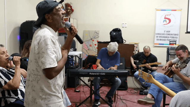 Hamilton Assunção canta ao microfone durante ensaio da banda Harmonia Enlouquece no Centro Psiquiátrico do Rio de Janeiro, cercado por outros integrantes tocando teclado e violão