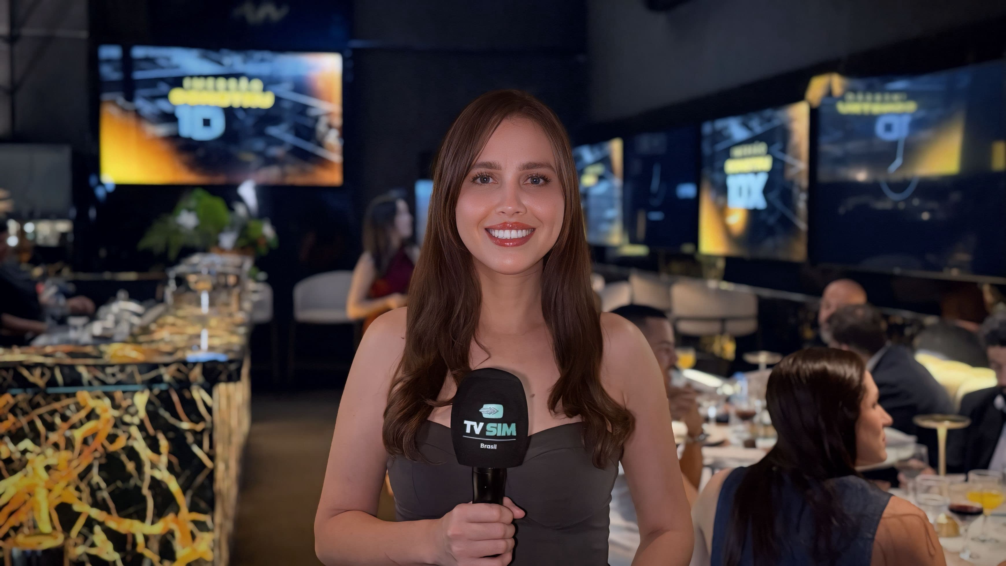 Repórter da TV Sim Brasil com microfone durante jantar corporativo no espaço de eventos