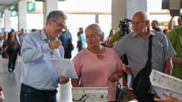 Servidor do TSE mostra documento a eleitores ao lado de urna eletrônica em ação educativa na rodoviária de Brasília