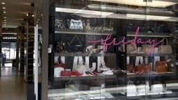 Vitrine de loja de bolsos e calçados decorada com letreiro de Black Friday, com pessoas refletidas no vidro