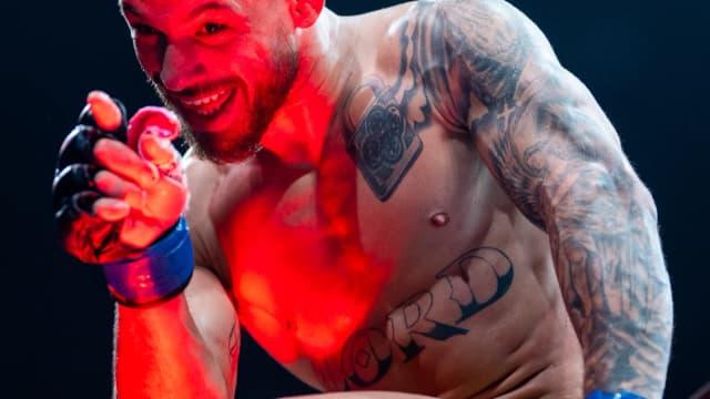 Lutador de MMA com o punho erguido durante entrada no octógono, iluminado por luz vermelha