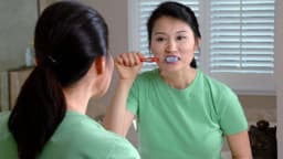 Mulher escovando os dentes em frente ao espelho
