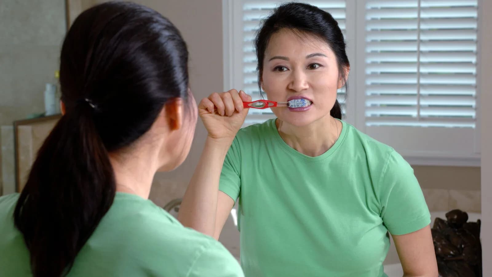 Mulher escovando os dentes em frente ao espelho