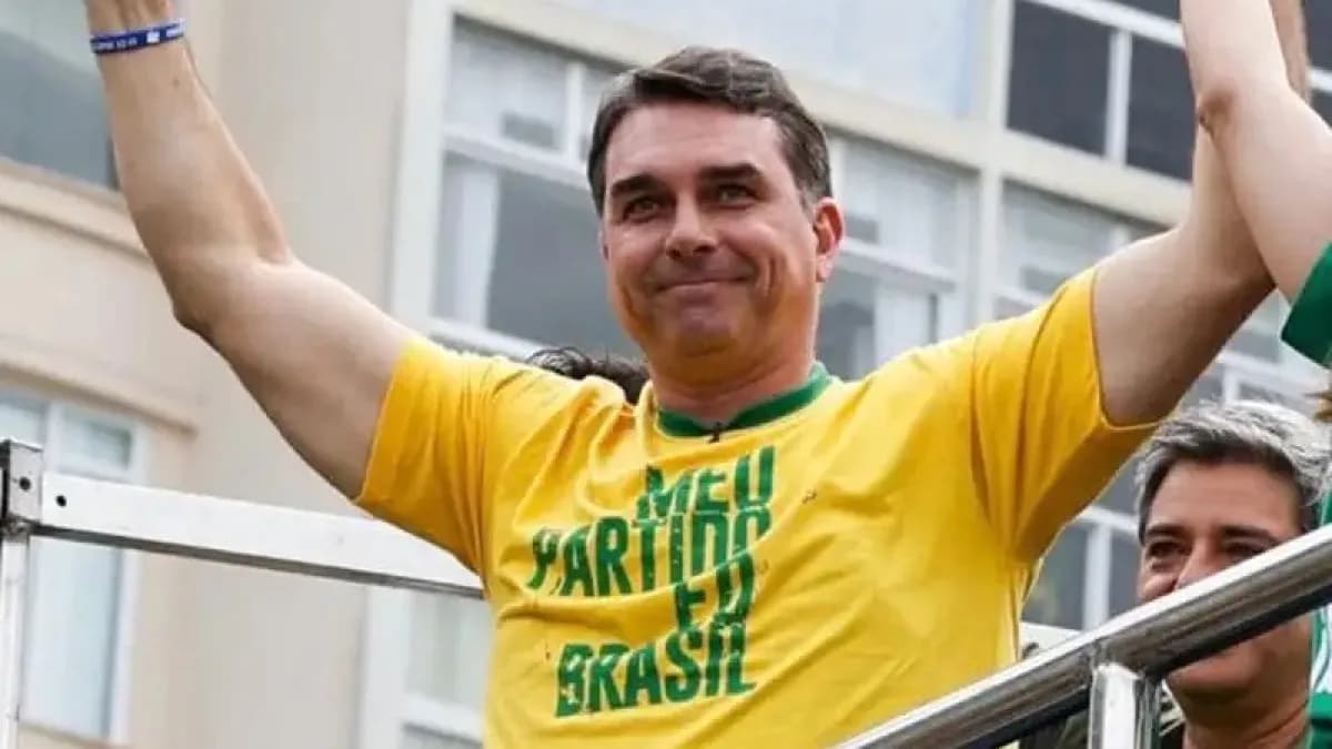 Flávio Bolsonaro acena para apoiadores durante ato de campanha, vestindo camiseta amarela e verde