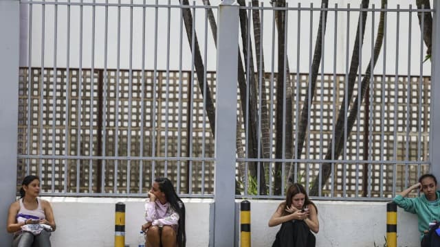 Candidatos sentados em banco de concreto aguardam do lado de fora de local de prova
