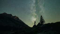Foto de arquivo feita na Suíça em que uma pessoa, em silhueta sobre uma pedra, observa o céu estrelado com a Via Láctea ao fundo, entre montanhas