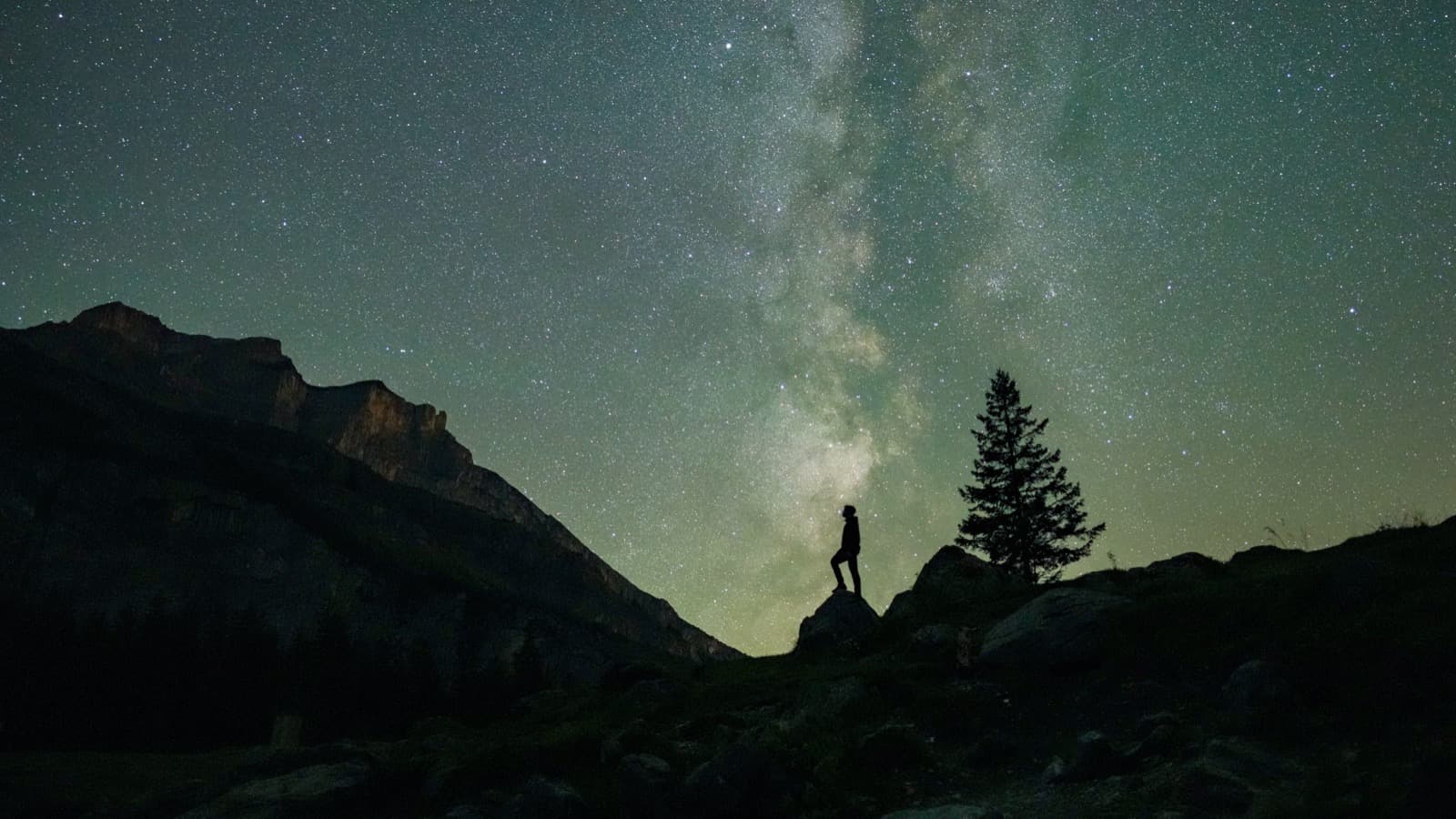 Foto de arquivo feita na Suíça em que uma pessoa, em silhueta sobre uma pedra, observa o céu estrelado com a Via Láctea ao fundo, entre montanhas