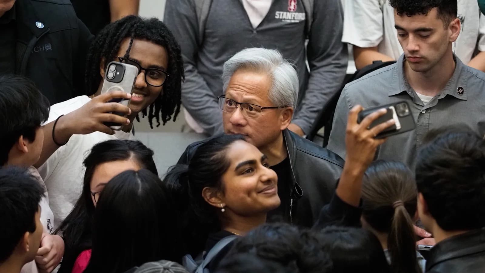 Jensen Huang, CEO da Nvidia, cercado por estudantes que tiram fotos com ele após palestra em Stanford