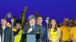 O presidente da Argentina, Javier Milei, discursa ao microfone no palco da convenção do PL, em São Paulo, cercado por apoiadores de camisa amarela que filmam com celulares