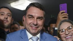 Senador Flávio Bolsonaro sorri cercado de apoiadores em evento de campanha