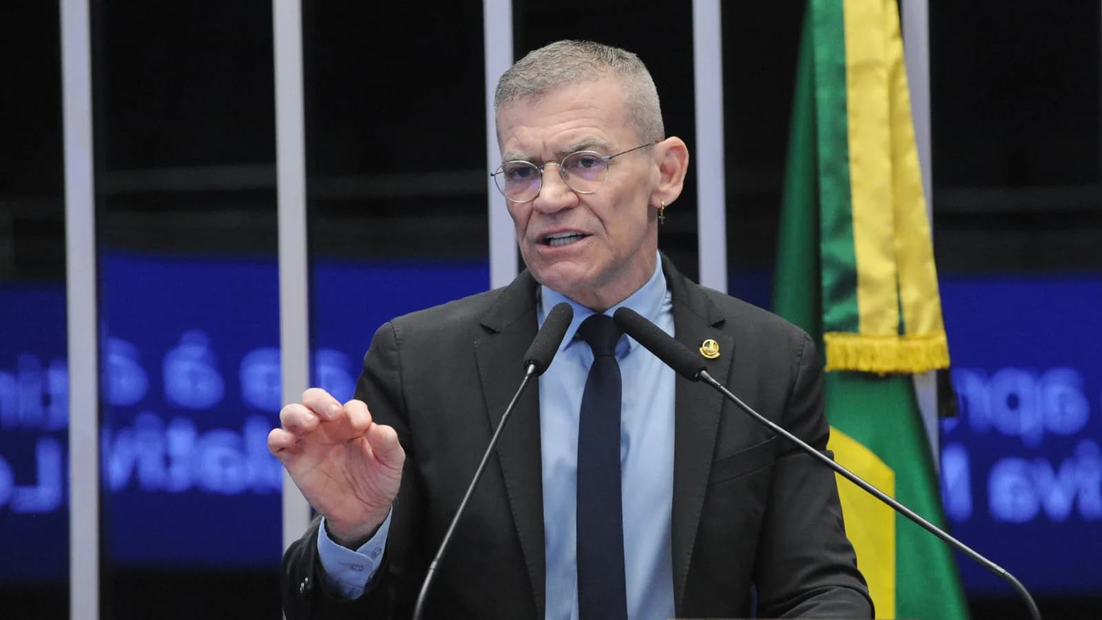 Senador Fabiano Contarato discursa em tribuna com a bandeira do Brasil ao fundo