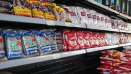Prateleira de supermercado com pacotes de arroz e feijão, itens da cesta básica