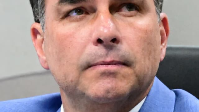 Flávio Bolsonaro de terno azul, olhando para cima, em sessão de comissão no Senado
