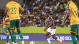 Jogadores em campo durante partida de futebol, com um deles conduzindo a bola cercado por adversários de uniforme amarelo e verde
