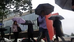 Pedestres andam sob chuva com guarda-chuvas na Avenida Paulista, em São Paulo, com o MASP ao fundo