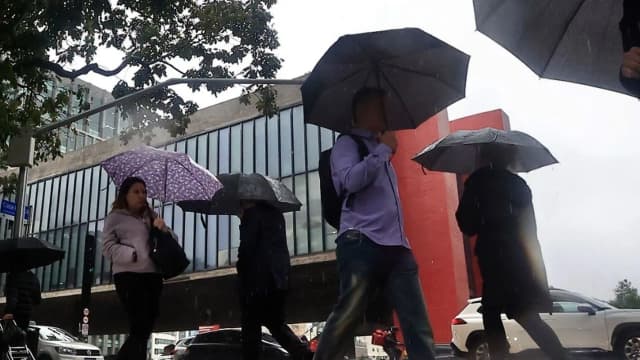 Pedestres andam sob chuva com guarda-chuvas na Avenida Paulista, em São Paulo, com o MASP ao fundo