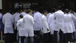 Grupo de médicos de jaleco branco reunidos na entrada de um centro de provas, foto de arquivo