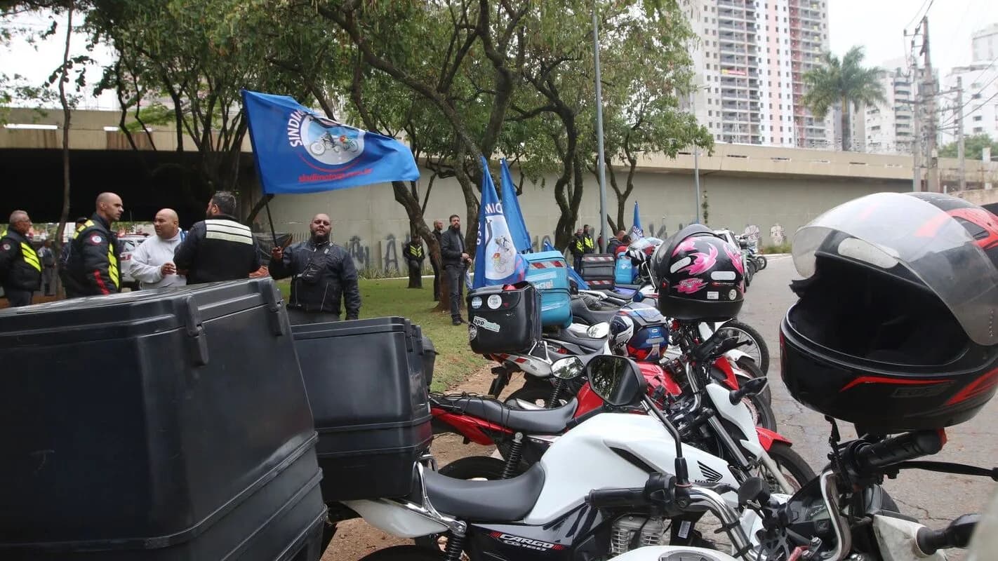 Entregadores com motocicletas e capacetes reunidos em ato do setor de delivery