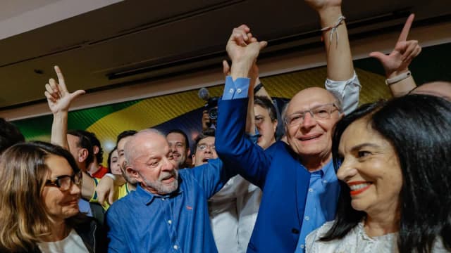 Lula sorri e acena com os braços levantados ao lado de apoiadores durante celebração da reeleição
