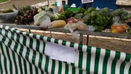 Banca de feira livre com verduras e legumes expostos, com aviso de papel escrito 'Pix' preso na barraca