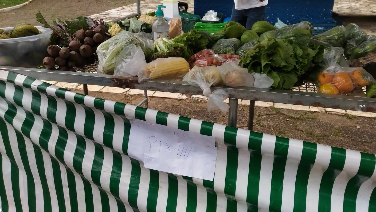Banca de feira livre com verduras e legumes expostos, com aviso de papel escrito 'Pix' preso na barraca