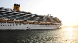 Navio de cruzeiro Costa Serena ao entardecer no porto de Santos, com passageiros no convés