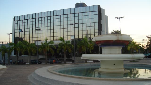 Fachada de prédio espelhado com palmeiras e chafariz em frente, em Rio Branco, no Acre
