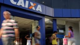 Fachada de agência bancária da Caixa com pessoas passando na calçada