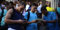 Grupo de candidatos consultando documentos e celular em fila do lado de fora de prédio público, foto de arquivo ilustrativa de concurso público