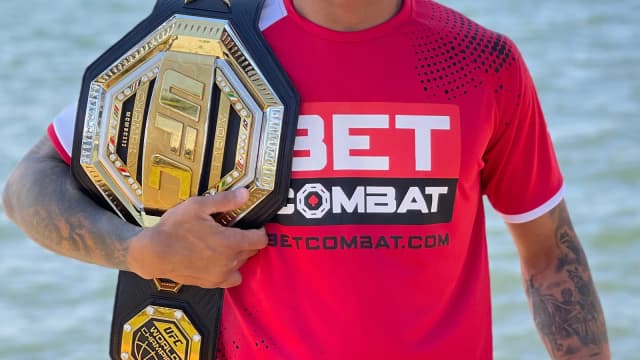Charles Oliveira sorri segurando o cinturão de campeão do UFC