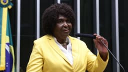 Benedita da Silva discursa com microfone na Câmara dos Deputados, vestindo blazer amarelo