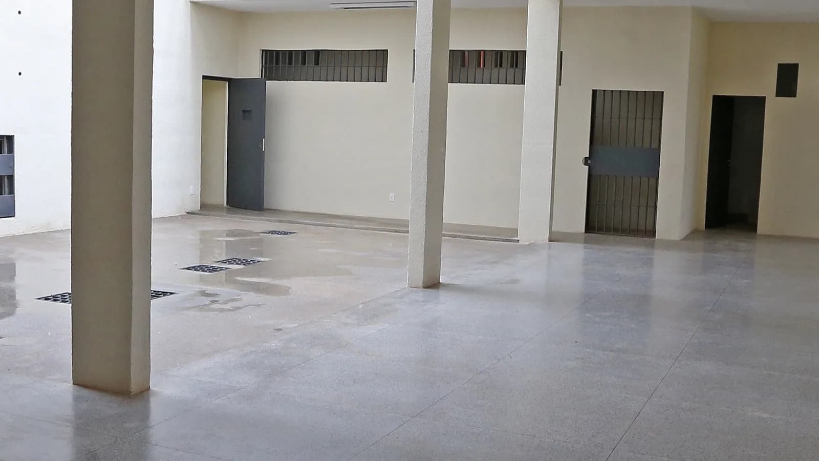 Corredor interno da penitenciária federal de segurança máxima de Brasília, com portas de grade e bancos de concreto