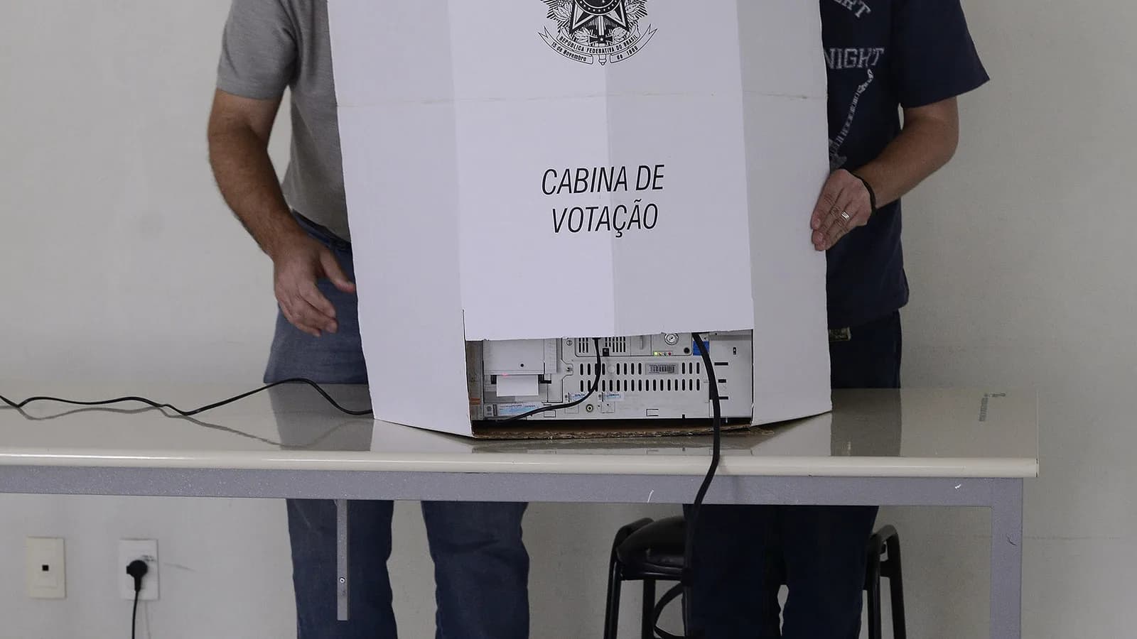Mesário auxilia eleitor em cabine de votação da Justiça Eleitoral