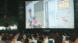 Público assiste a exibição de filme ao ar livre à noite, em sessão de cinema comunitário no Rio de Janeiro