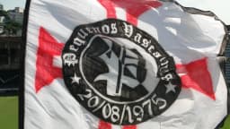 Bandeira da torcida organizada Pequenos Vascaínos tremulando em estádio, com o símbolo do Vasco da Gama ao centro
