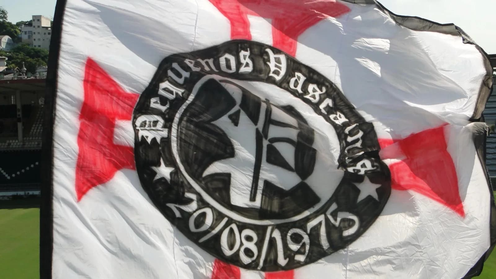Bandeira da torcida organizada Pequenos Vascaínos tremulando em estádio, com o símbolo do Vasco da Gama ao centro