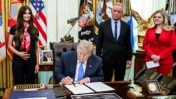 Donald Trump assina um documento sentado à mesa no Salão Oval da Casa Branca, cercado por assessores