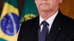 Jair Bolsonaro em retrato oficial, de terno escuro, diante de bandeiras