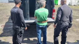 Policiais penais escoltam detento ao lado de viatura durante operação prisional
